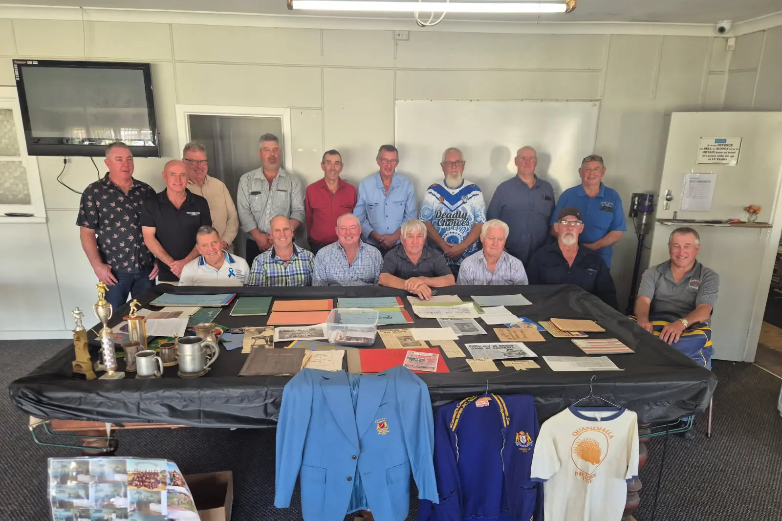 <p>Quandialla Echidna players over the years standing: Mark Troth, Brian Davidson, Danny Reeves, Chris Dixon, Chris Causer, Bruce Slade, Micheal Pearse, Phillip Armitage and Robert Reeves. 1976 Quandialla Echidnas premiership players seated: Bruce Barrett, Lewis Heinjus, Ian Murphy, Ted Langford, Harry Gault, Ian Nixon and Ken Slade surrounded by Quandialla Echidnas memorabilia. </p>\\n